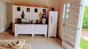 Una cocina compacta con armarios blancos, cafetera y refrigerador. Se aprecia una pequeña ventana con vistas a la vegetación.