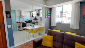 A modern kitchen with a dining area, a sofa with yellow cushions, and artwork on the walls. - COBAR0110 - Edifício Beta (Salvador)