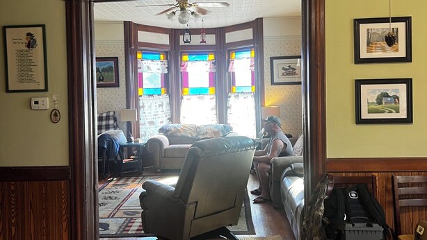 A room with a wooden floor, a ceiling fan, and a view through a doorway to a living area with a sofa, a chair, and a table. - 110 year old Renovated farm house in the heart of Cawcker city (Cawker City)