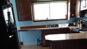 A kitchen with wooden cabinets, a large window, a wooden countertop, and a black refrigerator. - 110 year old Renovated farm house in the heart of Cawcker city (Cawker City)