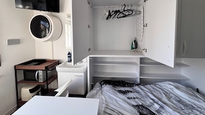 A compact bedroom with a bed, a built-in TV, a small kitchenette, and a storage cabinet.