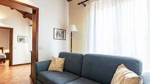 Un salon avec un canapé gris, deux coussins, une lampe sur pied et un tableau encadré accroché au mur.