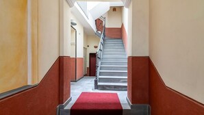 Un escalier recouvert d’une moquette rouge mène à un palier, de part et d’autre duquel se dressent des murs à la finition texturée.