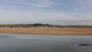Un paisaje costero con una playa arenosa, agua tranquila y un pueblo distante con edificios y vegetación.