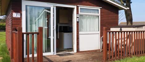 A small, single-story cabin with a sliding glass door entrance, a small kitchen area, and a fenced deck.