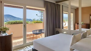 Une chambre d’hôtel avec un grand lit, un balcon donnant sur les collines et un bureau avec une chaise.