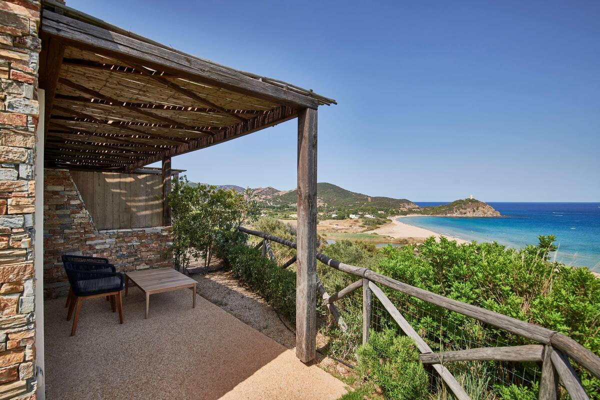Un bâtiment en pierre doté d’une pergola en bois et d’un espace détente offrant une vue sur une plage et l’océan.