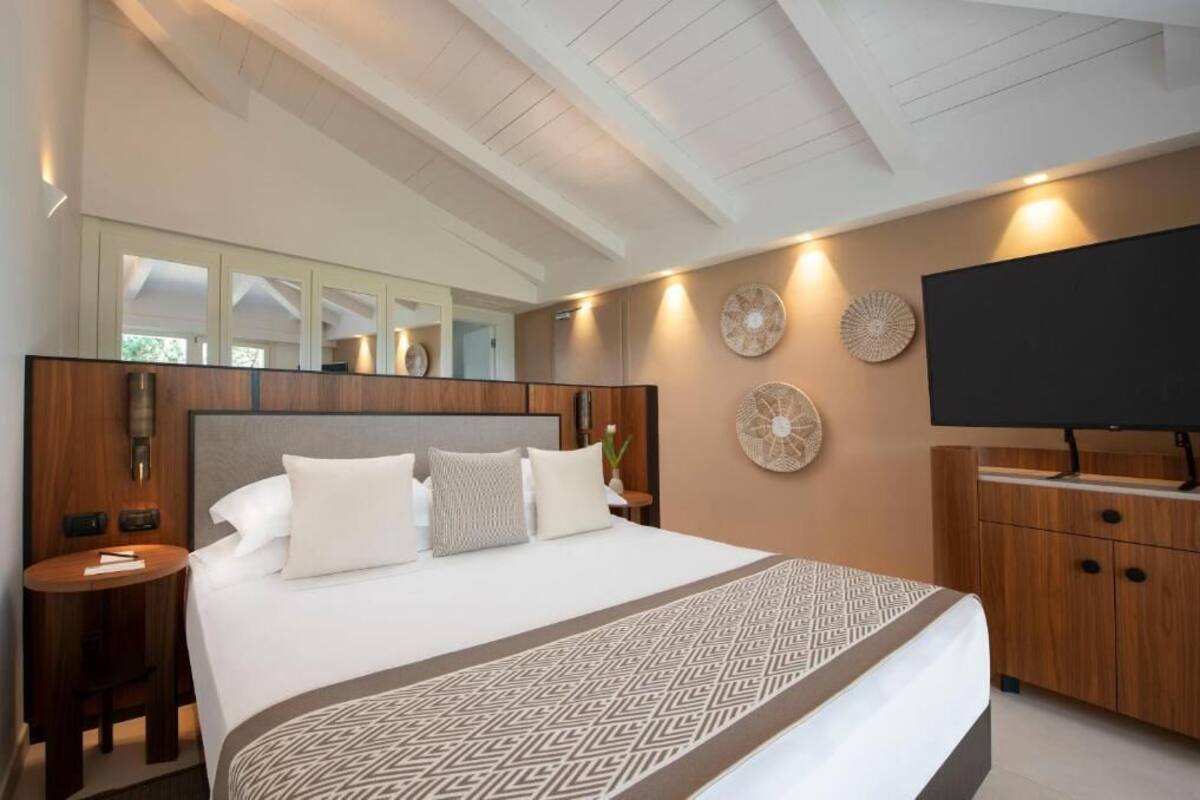Une chambre d’hôtel moderne dotée d’un grand lit, d’une tête de lit en bois, de tables de chevet, d’un téléviseur à écran plat et de décorations murales.
