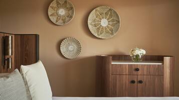Un dormitorio con un aparador de madera, una cama con ropa blanca y tres piezas de decoración mural tejida.