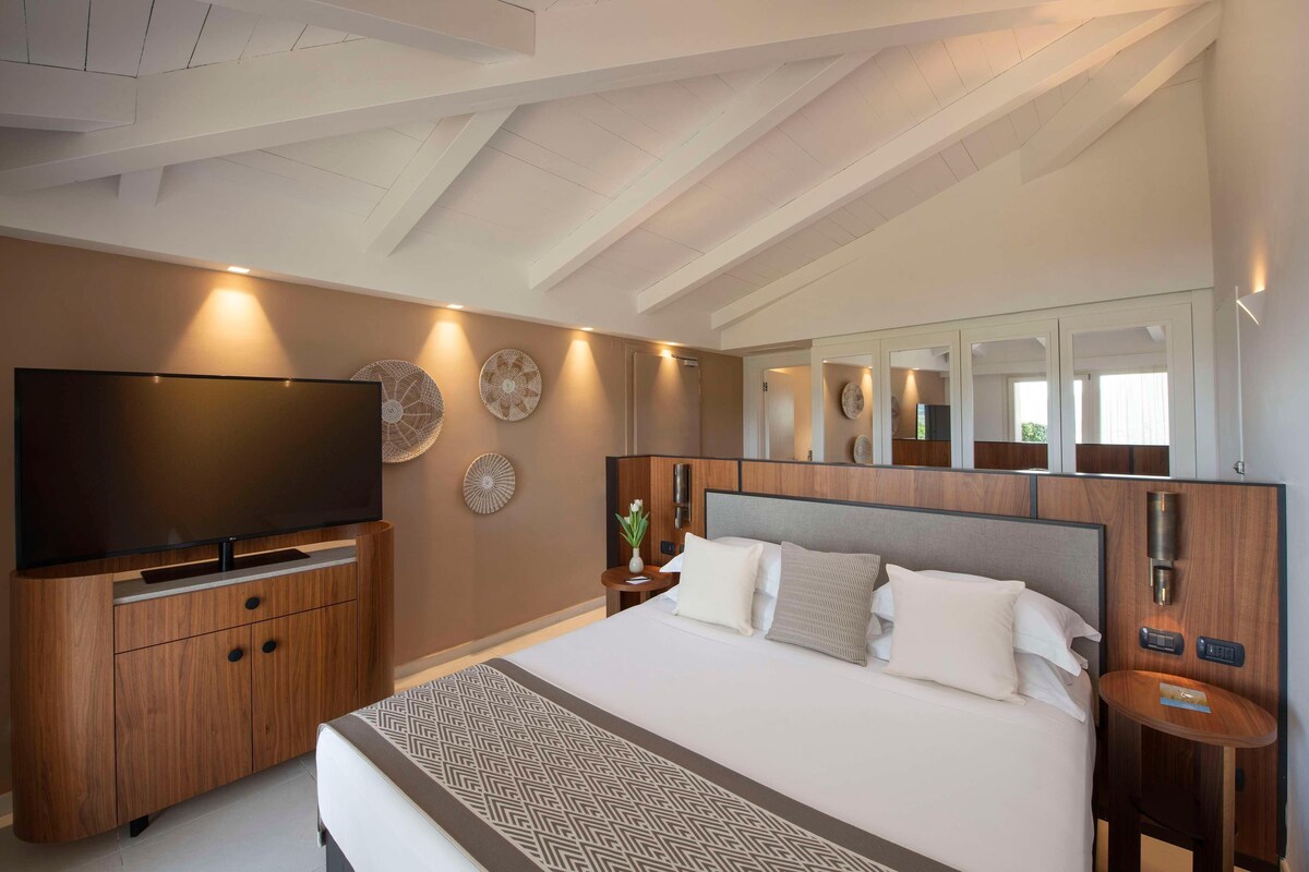 Een moderne hotelkamer met een groot bed, een flatscreen televisie, houten meubels en een plafond met zichtbare balken.