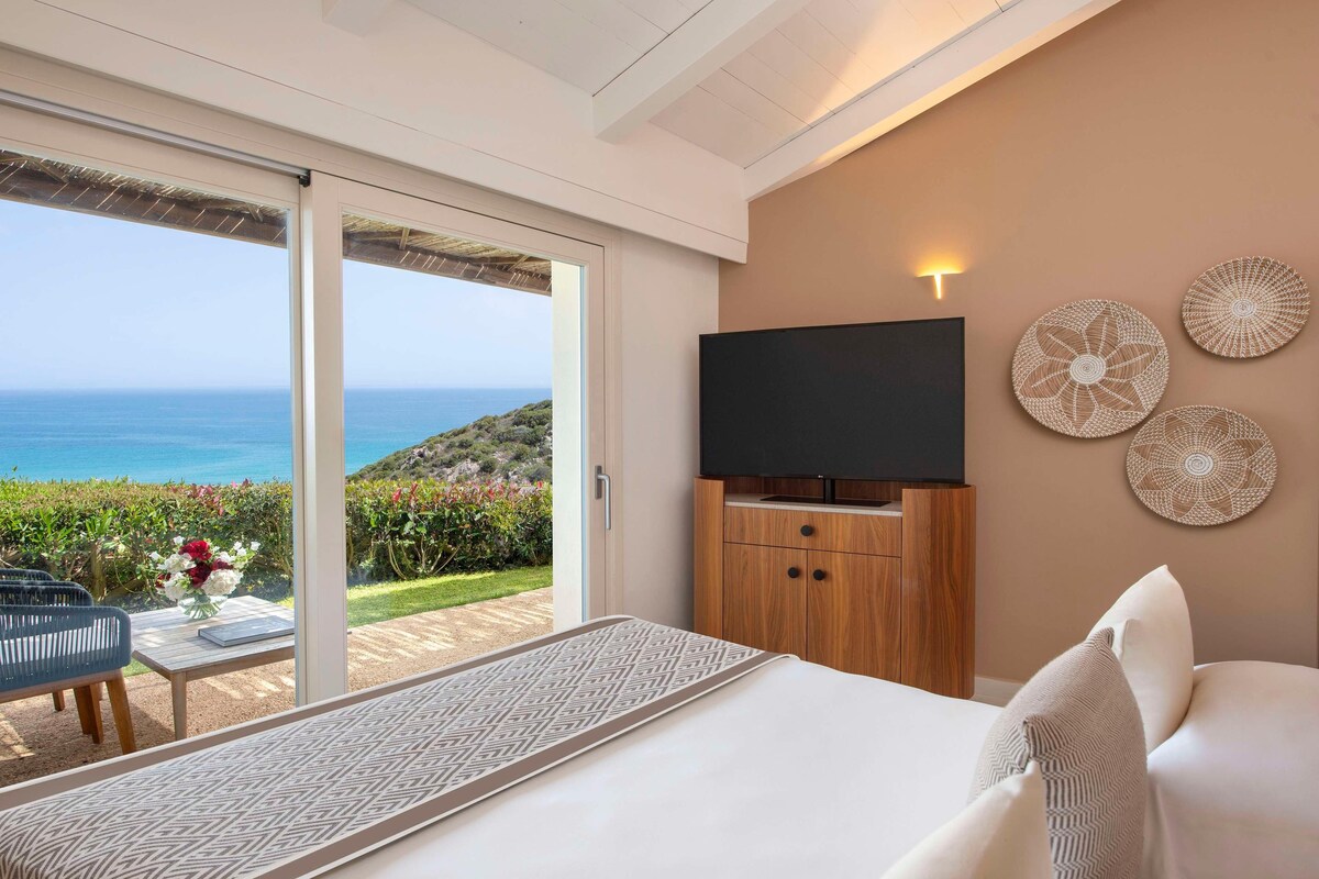 Habitación de hotel con cama, televisión y vista al océano.