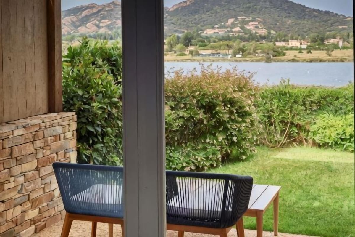 A patio with a view of a lake and mountains, a brick wall, and two wicker chairs.