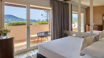 Een hotelkamer met een groot bed, een balkon met uitzicht op de heuvels, en een bureau met een stoel.