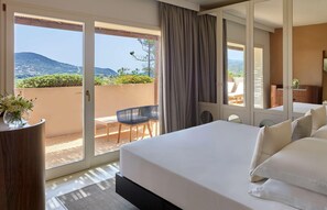 A hotel room with a large bed, a balcony with a view of the hills, and a desk with a chair. - Baia di Chia Resort Sardinia, Curio Collection (Domus de Maria)