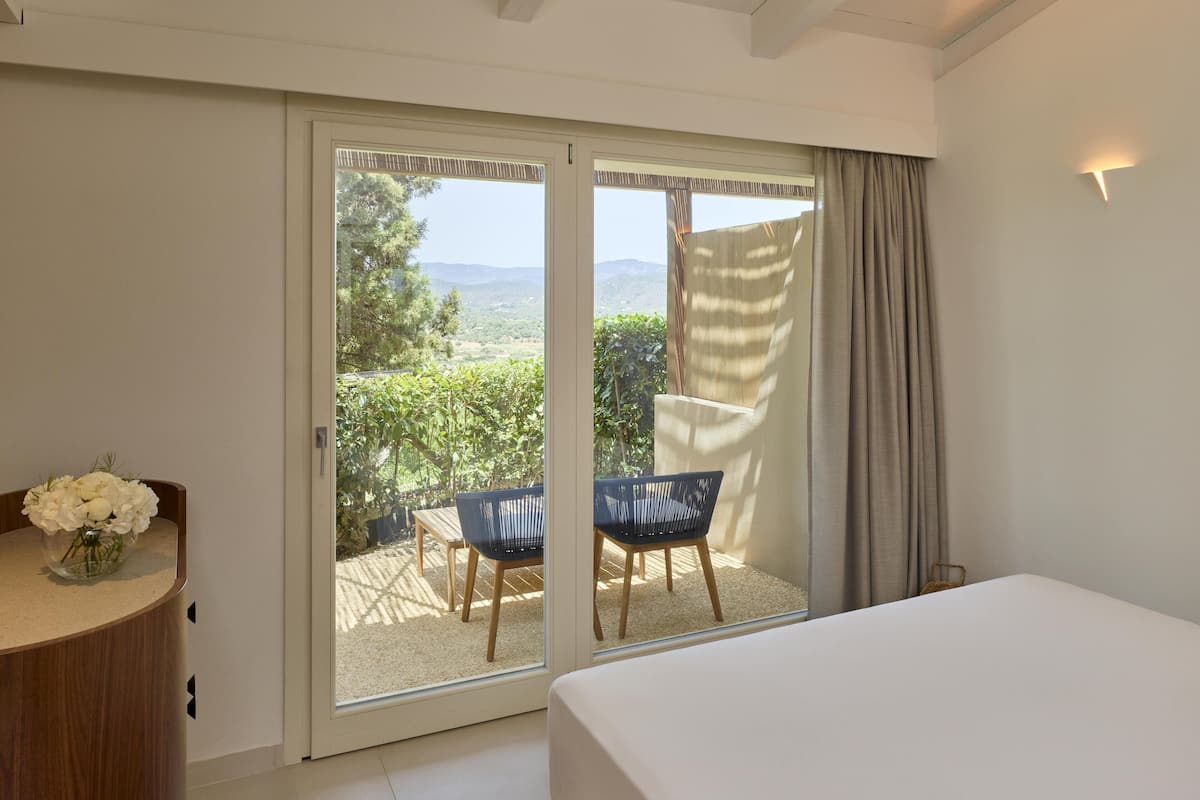Une chambre avec un lit, une chaise, une table et une vue sur un espace extérieur accessible par une porte coulissante, où se trouvent une table et une chaise.