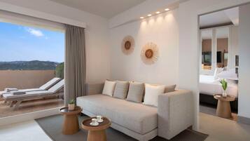 Une chambre d’hôtel moderne avec un canapé, deux tables d’appoint, une petite table ronde avec des tasses, une plante en pot et une vue sur l’extérieur.