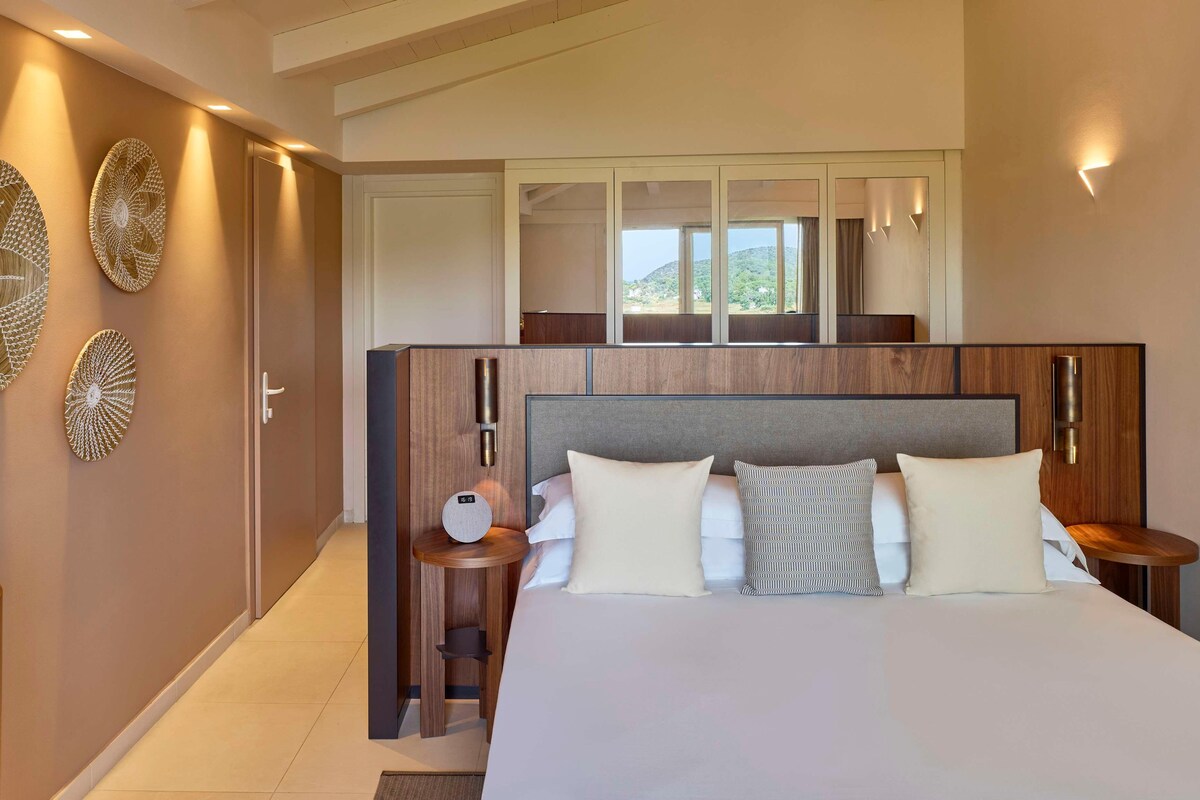 Een moderne hotelkamer met een groot bed, een houten hoofdeinde, een nachtkastje met een lamp en decoratieve wandkunst.