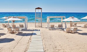 A beach wedding setup with a wooden archway, white umbrellas, and lounge chairs. - Baia di Chia Resort Sardinia, Curio Collection (Domus de Maria)