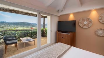 Una habitación con cama, televisor, mesa y silla. Hay una puerta corrediza de vidrio que da a un espacio exterior con vistas al campo.