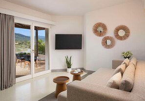 A modern living room with a sofa, a flat-screen TV, and a view of a patio with outdoor furniture. - Baia di Chia Resort Sardinia, Curio Collection (Domus de Maria)