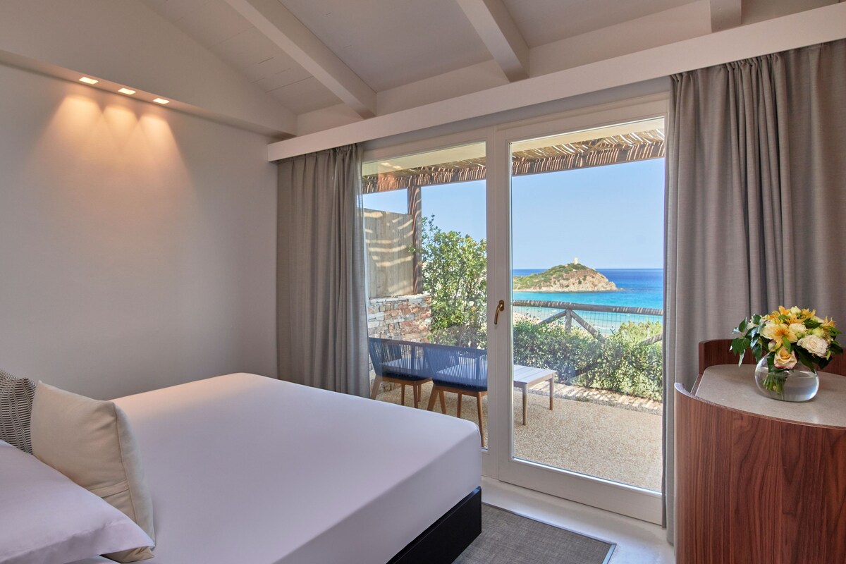 Een slaapkamer met een bed, uitzicht op zee en een balkon met een tafel en stoelen.