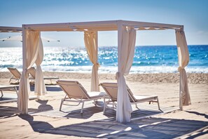 Eine Strandhütte mit Holzterrasse und weißen Vorhängen mit Blick aufs Meer.