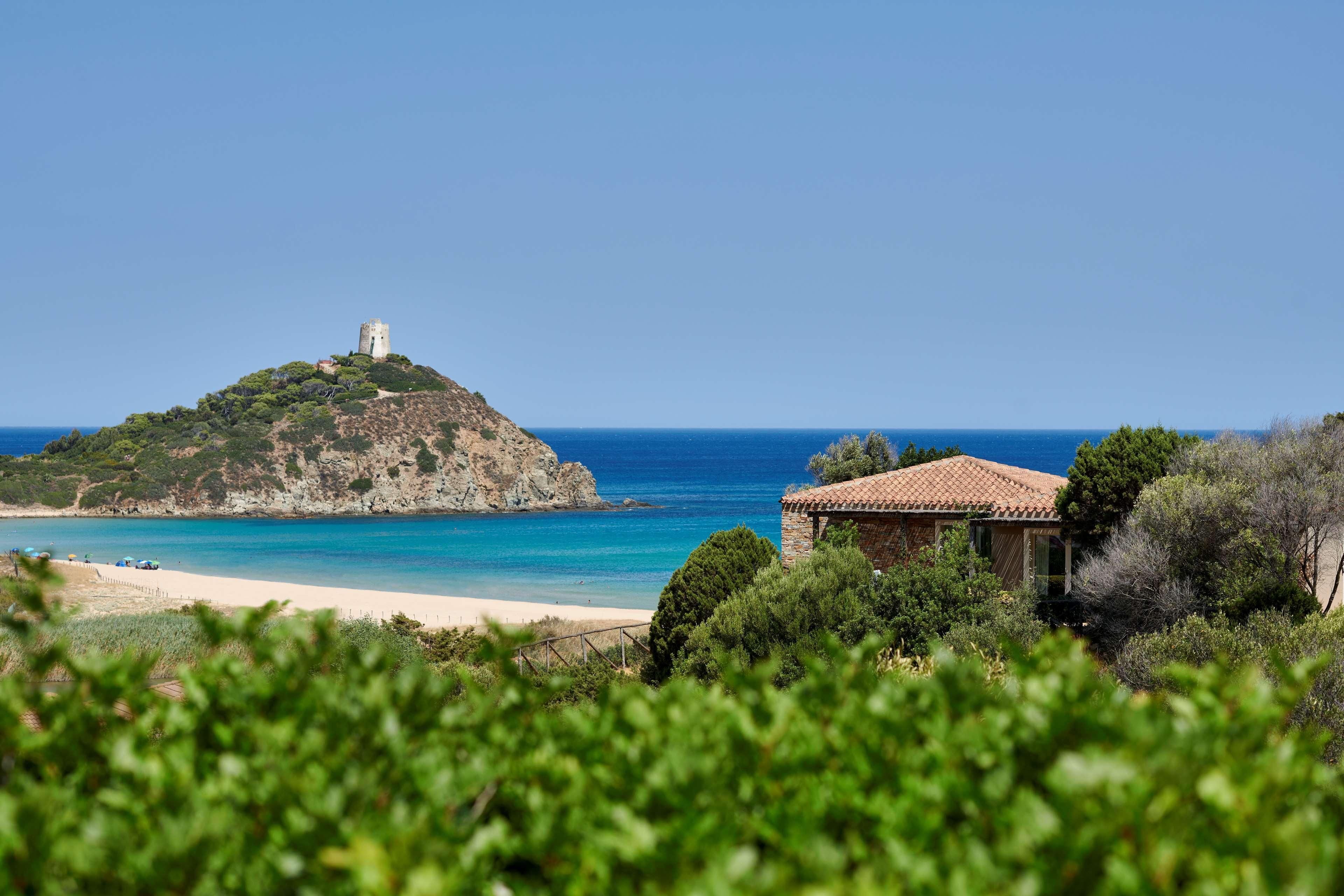 A coastal landscape with a hill featuring a tower, a beach, and a building with a tiled roof.