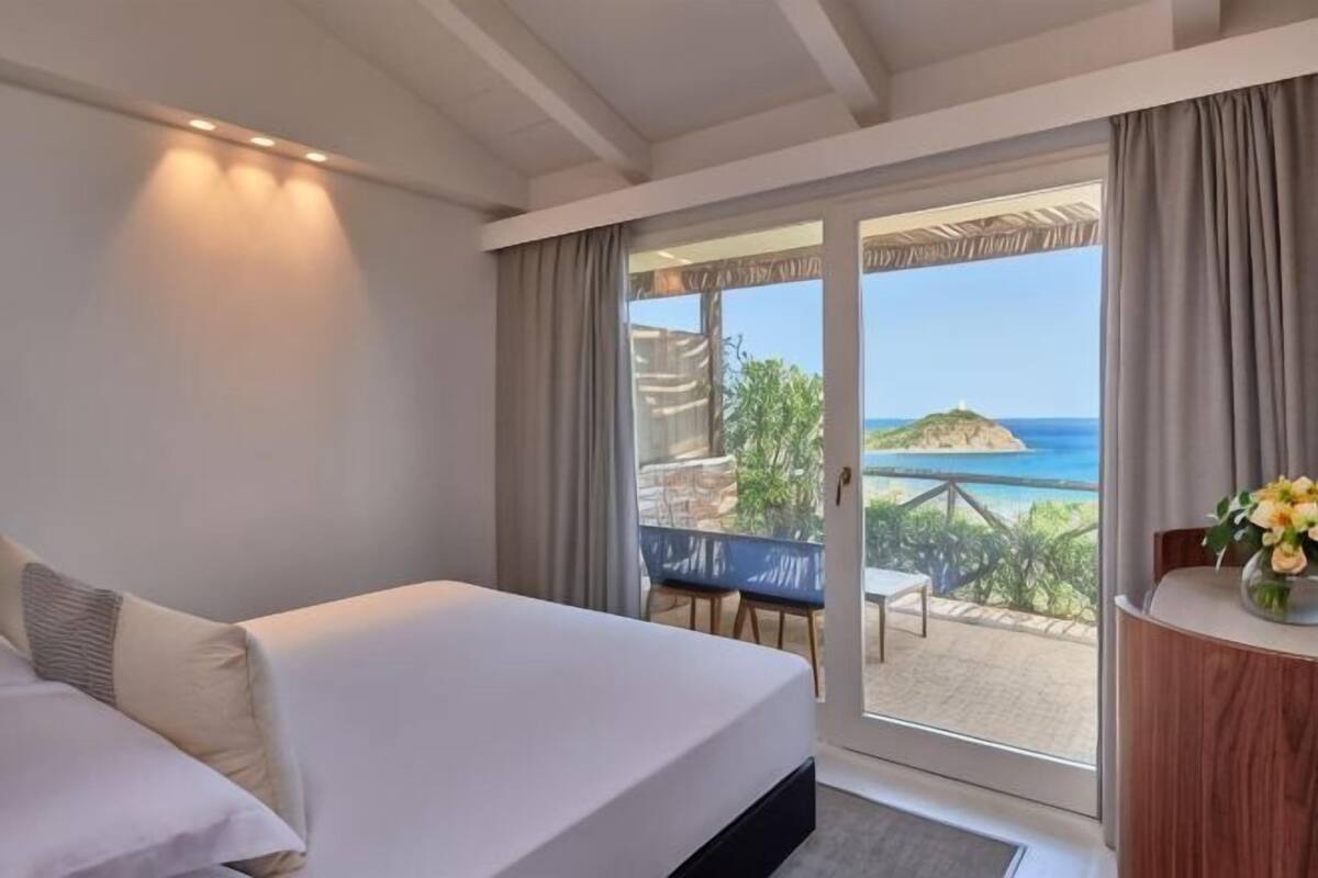 Une chambre d’hôtel avec un lit, une vue sur la mer et un balcon équipé d’une table et de chaises.