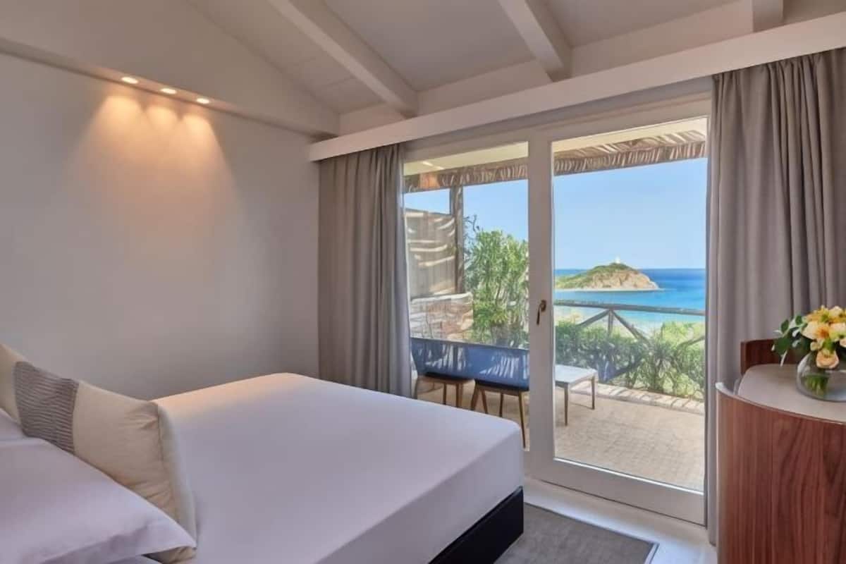 A hotel room with a bed, a view of the sea, and a balcony with a table and chairs.