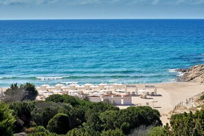 A beachside property with multiple beach huts and umbrellas, a sandy beach, and a view of the ocean. - Baia di Chia Resort Sardinia, Curio Collection (Domus de Maria)