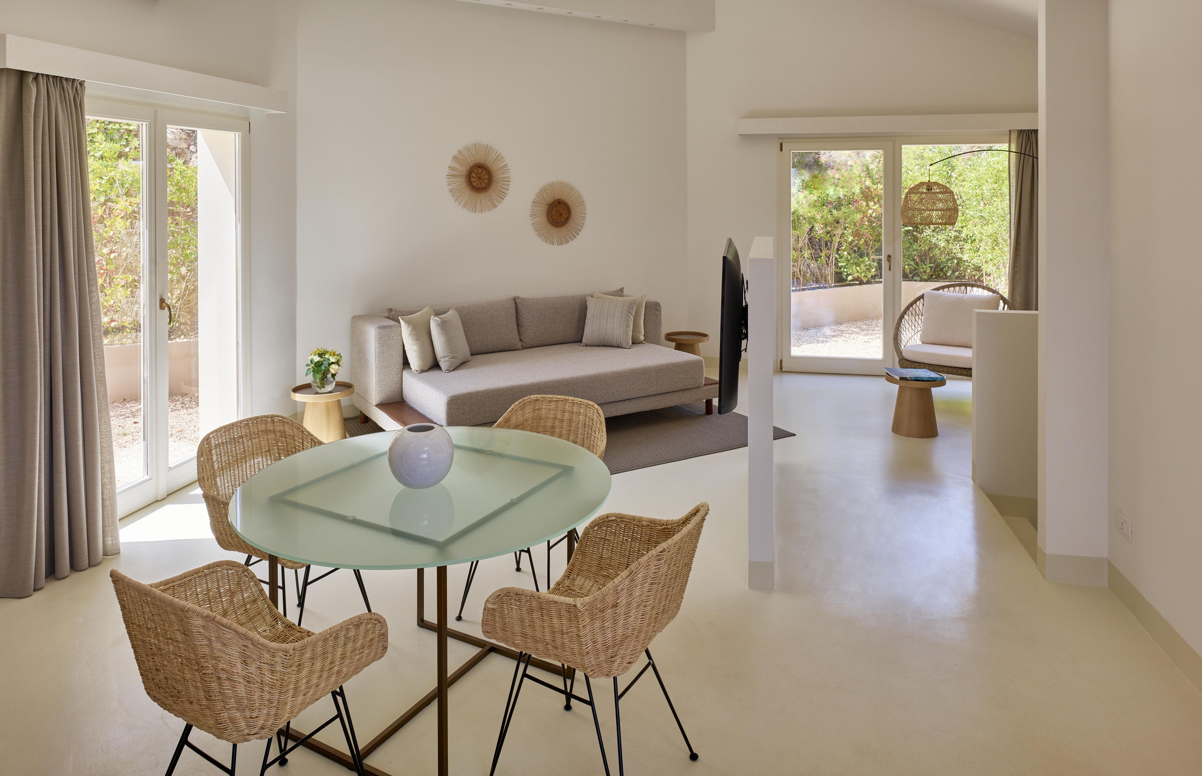 A modern living room with a glass table, wicker chairs, a sofa, and a TV.