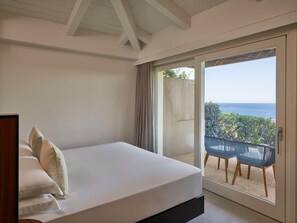 Un dormitorio con una cama, vista al mar a través de un ventanal corredero y un balcón con sillas.