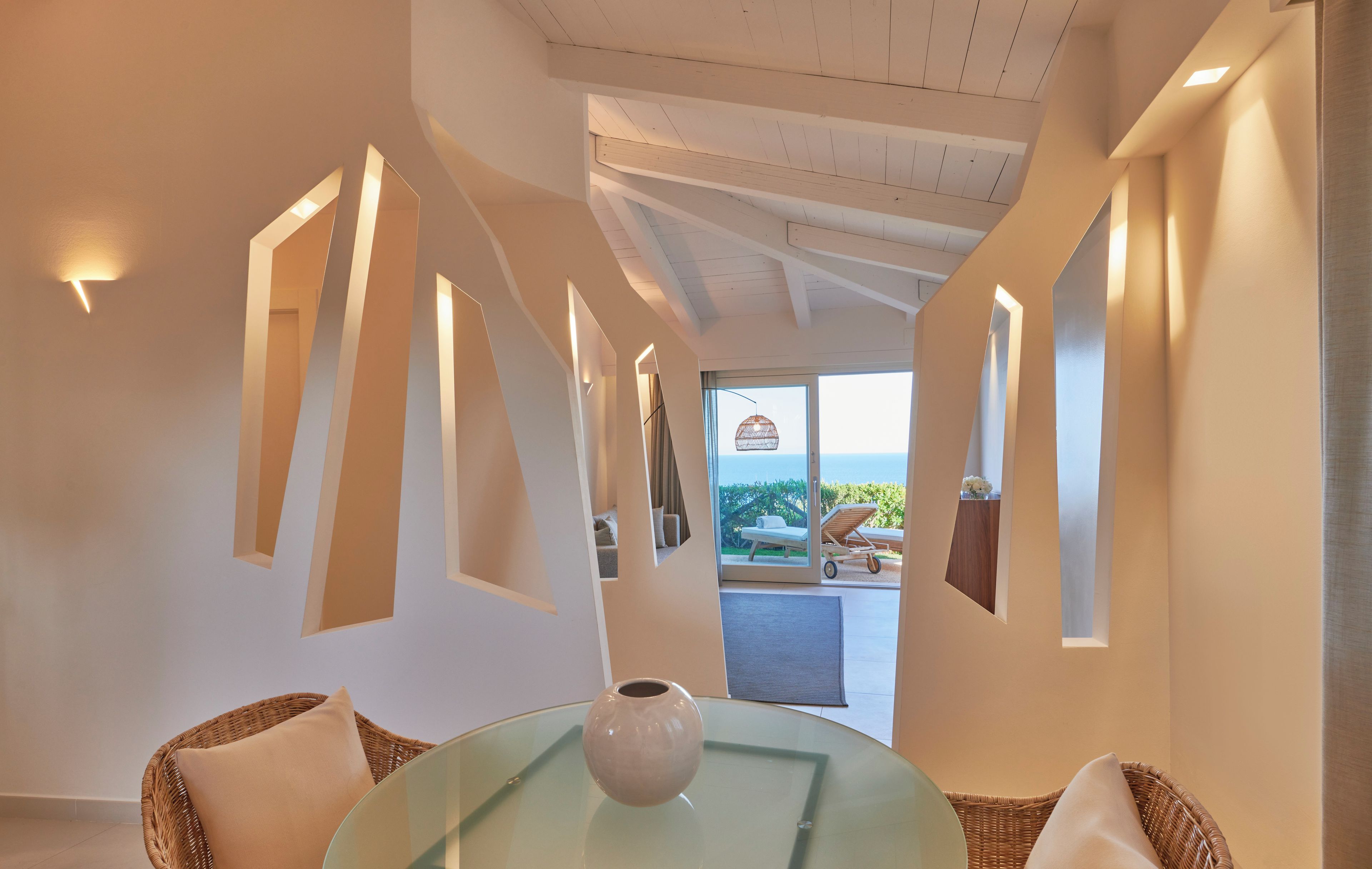 A modern interior with a glass table, wicker furniture, and a view of the outdoors.