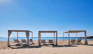 A beach with three open-air structures, each with a pair of lounge chairs. - Baia di Chia Resort Sardinia, Curio Collection (Domus de Maria)