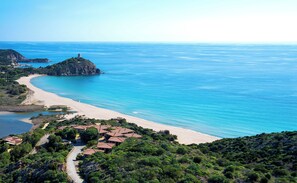 Eine Küstenlandschaft mit Strand, einem Turm auf einer kleinen Insel und einer Häusergruppe mit roten Dächern.