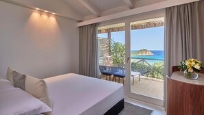 Une chambre avec un grand lit, une vue sur la mer et un balcon équipé d’une table et de chaises.