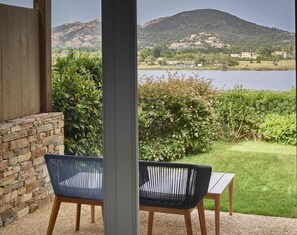 A patio with two chairs and a table, overlooking a lake and hills. - Baia di Chia Resort Sardinia, Curio Collection (Domus de Maria)