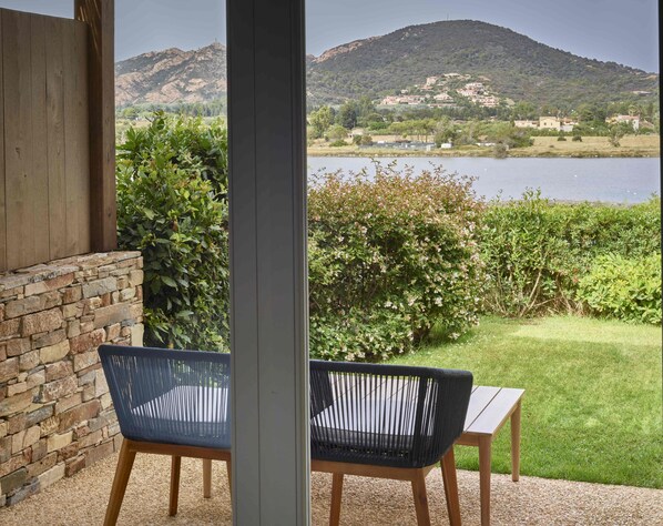 A patio with two chairs and a table, overlooking a lake and hills. - Baia di Chia Resort Sardinia, Curio Collection (Domus de Maria)