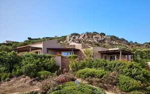 Una villa en una ladera con fachada de piedra, varias habitaciones y vistas del paisaje circundante.