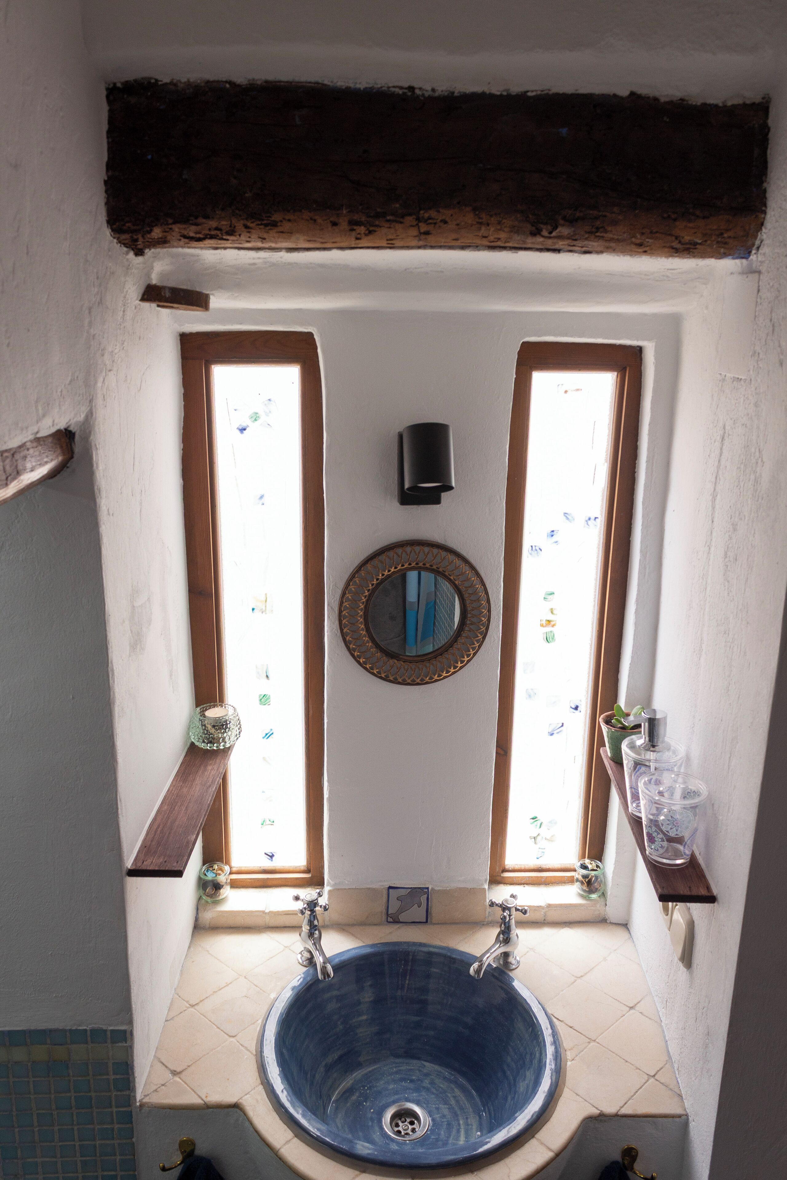 Un bagno con un lavandino blu, due finestre, uno specchio e uno scaffale con articoli da toilette.