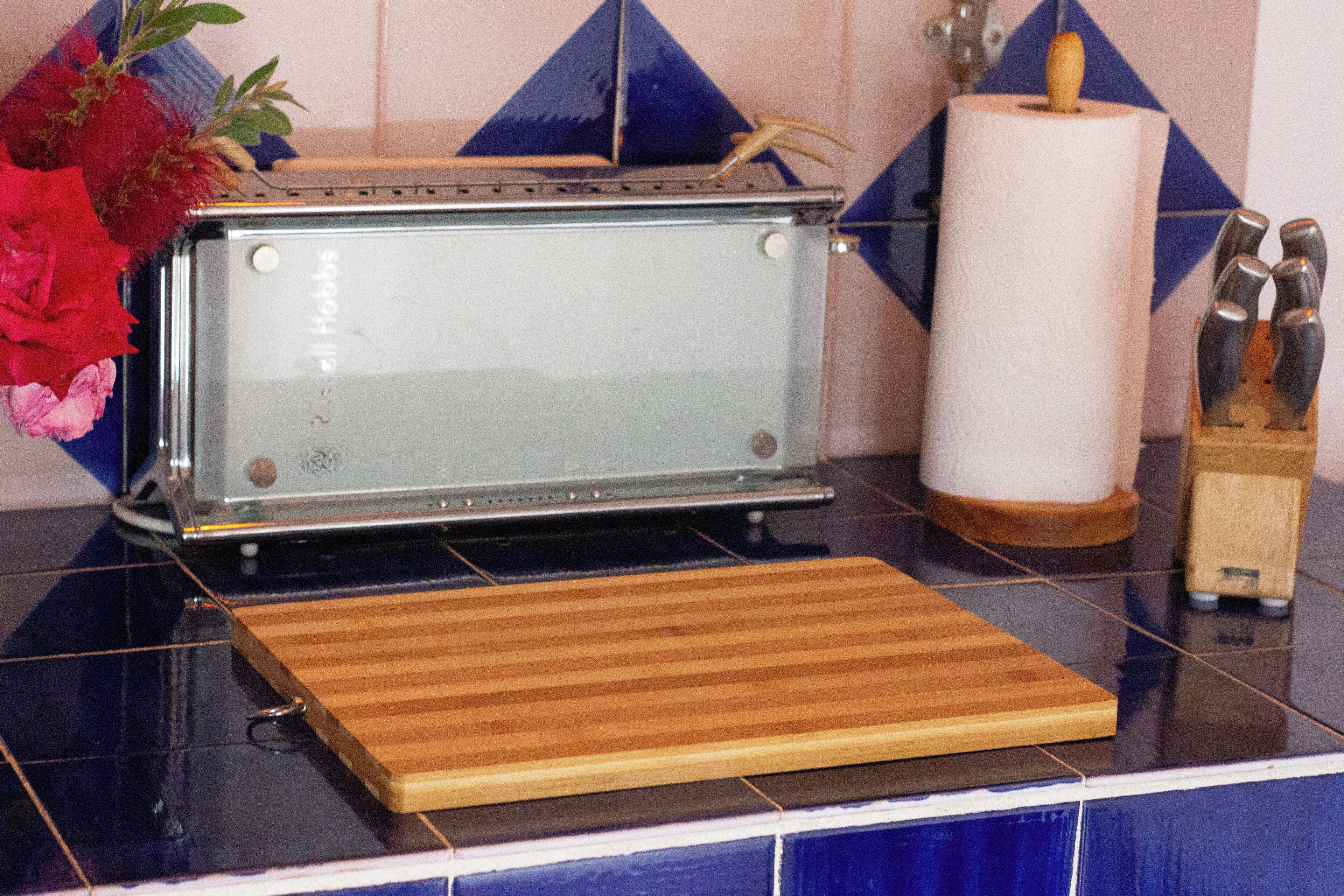 A kitchen with a toaster, a wooden cutting board, a roll of paper towels, and a knife block.