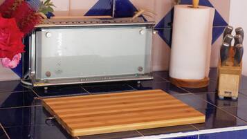 A kitchen with a toaster, a wooden cutting board, a roll of paper towels, and a knife block.