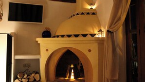 A fireplace with a stone arch, a wooden shelf with logs, and a wall-mounted television.