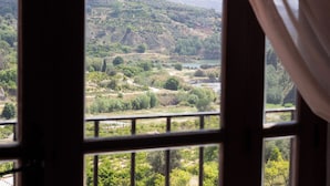 A view through a window with a metal frame, revealing a landscape with hills, trees, and a body of water.