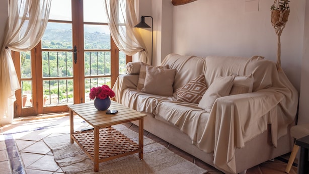 A cozy living room with a beige sofa, a wooden coffee table, and a view through large windows.