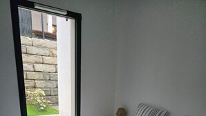 Une chambre à coucher avec un lit, des oreillers, une table de chevet, une lampe et une vue sur un mur de pierre et la verdure à l’extérieur.