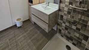 Une salle de bain moderne avec un grand miroir, des meubles en bois, un lavabo blanc et une douche dont le mur arrière est recouvert de carreaux à motifs.