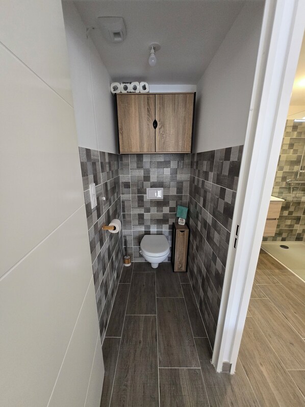 A compact bathroom with a toilet, a wooden cabinet above, and a tiled backsplash.