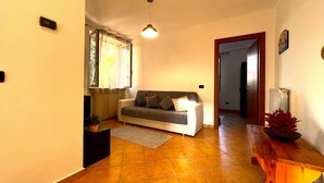 A living room with a sofa, a small table, a potted plant, and a window with curtains. - Apartment in the center of Serravalle at 5min from the outlet Serravalle Mcarthurglen (Serravalle Scrivia)