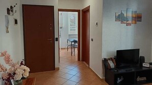 A hallway with a wooden door, a dining area with a table and chairs, and a black entertainment unit with a TV. - Apartment in the center of Serravalle at 5min from the outlet Serravalle Mcarthurglen (Serravalle Scrivia)